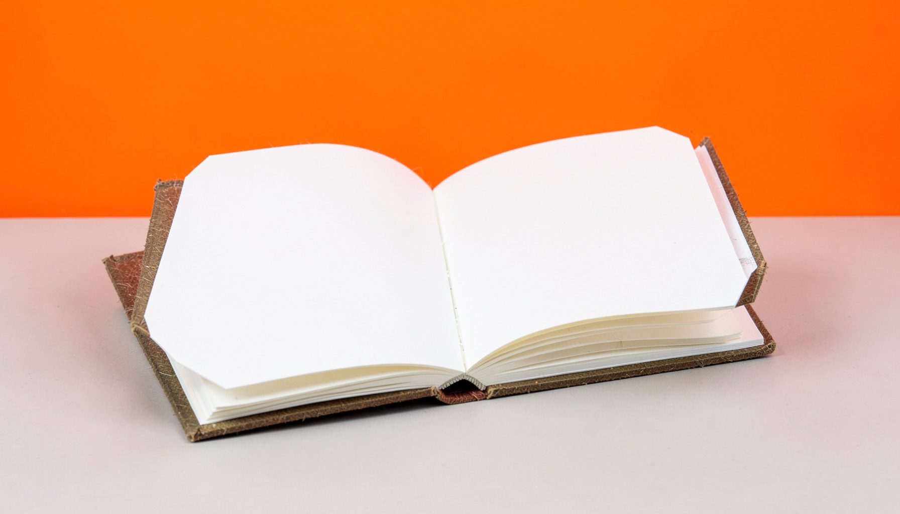 An open handmade photo album with blank pages and a textured cover, resting on a neutral studio surface